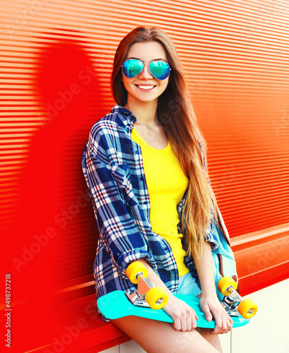 Portrait of happy smiling young woman with skateboard wearing colorful on vivid background