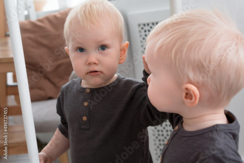 Little blond boy looking at himself reflection in mirror at home © Natalia Navodnaia