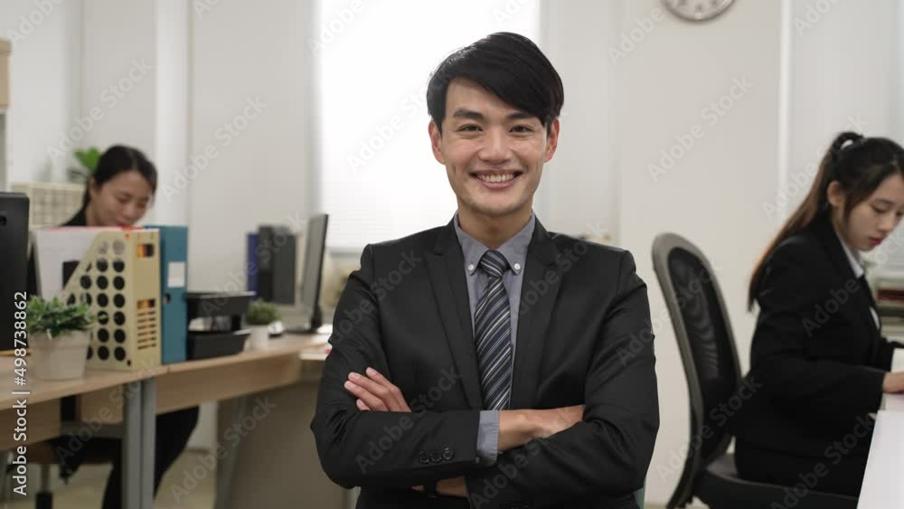 portrait of a successful asian male team leader wearing business suit looking at camera with smile and folded arms at modern workplace background with coworkers portrait of a successful asian male team leader wearing business suit looking at camera with smile and folded arms at modern workplace background with coworkers
