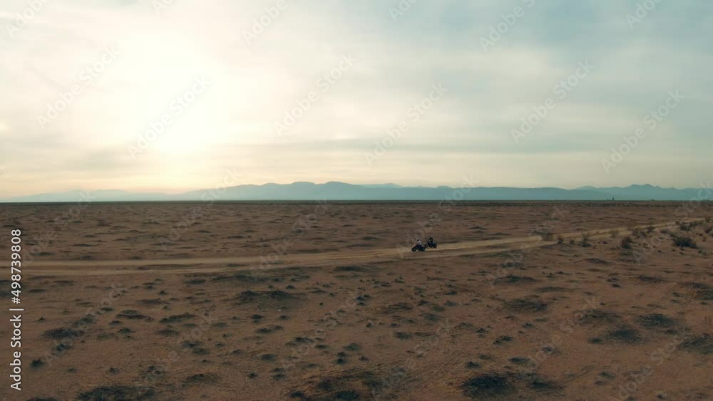 Riding three-wheeler trikes along a Mojave Desert dirt trail - sweeping aerial view at sunset Riding three-wheeler trikes along a Mojave Desert dirt trail - sweeping aerial view at sunset