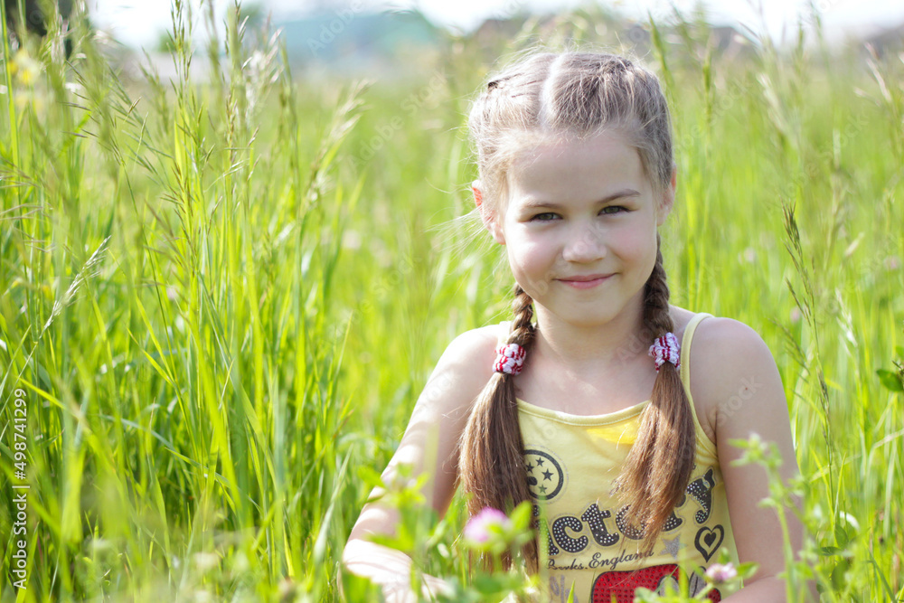 A little girl with pigtails sits on green grass in a summer park on a sunny day A little girl with pigtails sits on green grass in a summer park on a sunny day