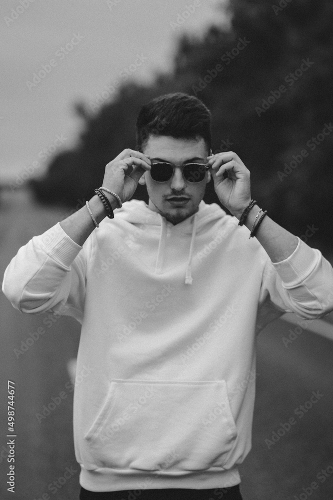 A young handsome guy with a small beard in a white jacket and dark glasses  is walking along the road. Black and white Stock Photo | Adobe Stock