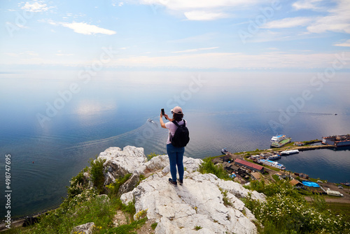 A female traveler stands on a rock near the port of Baikal and photographs Lake Baikal on a summer day. The concept of freedom, hiking.