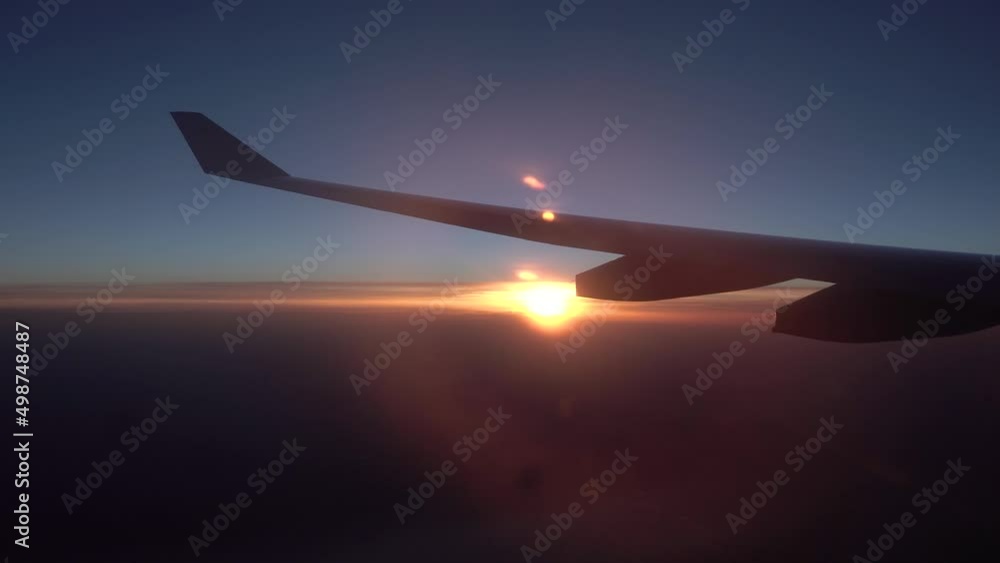 Aerial view of sunrise through airliner window. Airplane flight. Wing of an airplane flying above the clouds with sunset sky. View from the window of the plane. Airplane, Aircraft. sun on the horizon Aerial view of sunrise through airliner window. Airplane flight. Wing of an airplane flying above the clouds with sunset sky. View from the window of the plane. Airplane, Aircraft. sun on the horizon