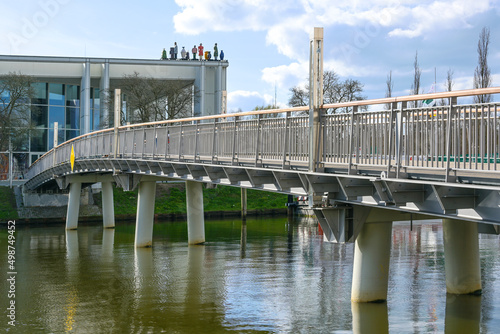 Pedestrian bridge to the Music and Congress Hall or MuK in Lubeck, Germany on the river Trave, modern building by Meinhard von Gerkan with sculptures called Strangers on the roof, blue sky with clouds