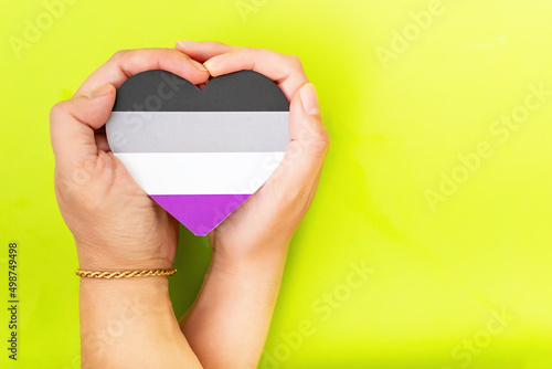 Woman hands hold heart in the colors of asexual flag on green background. LGBT concept, Pride month. Top view, copy space.