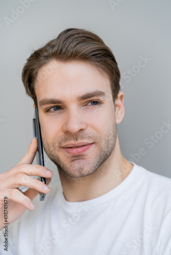 portrait of young man looking away during conversation on smartphone isolated on grey.