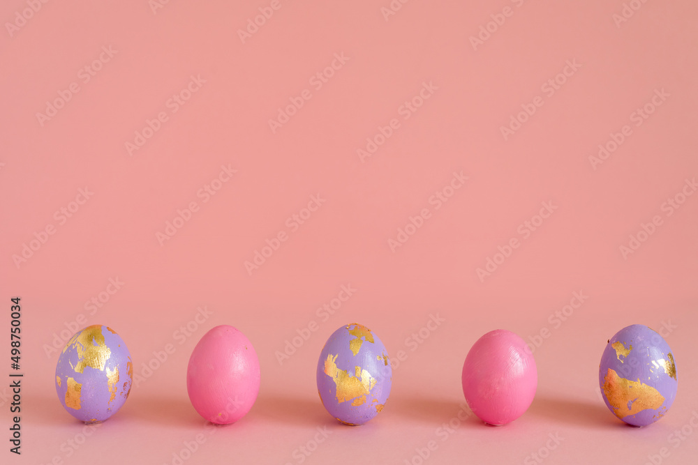 Easter eggs, pink and violet with golden foil on pink background, copy space.