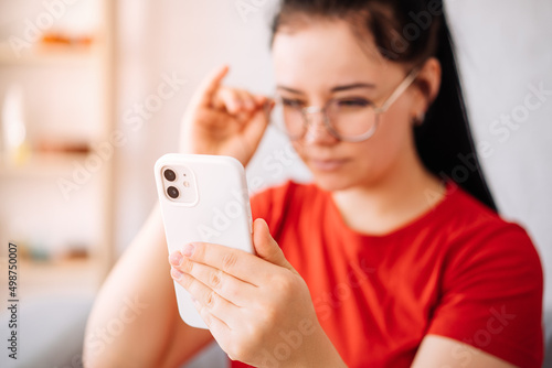 A girl with glasses with vision problems is trying to read a text on the phone at home. the girl has myopia. focus on the phone