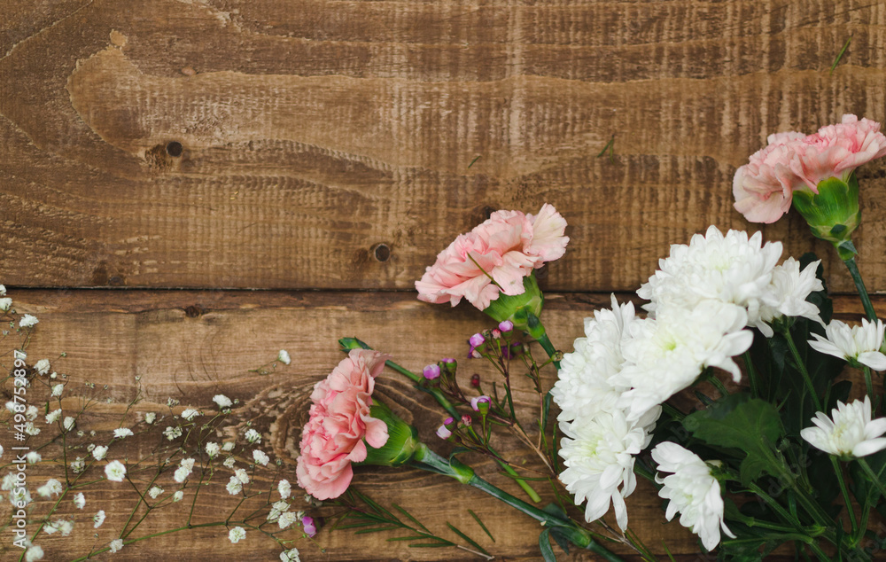 Flat lay closeup top view of a rustic wooden table on which various carnation flowers, chrysanthemum and gypsophila of colorful flowers are arranged in the corner, space for text. Flat lay closeup top view of a rustic wooden table on which various carnation flowers, chrysanthemum and gypsophila of colorful flowers are arranged in the corner, space for text.
