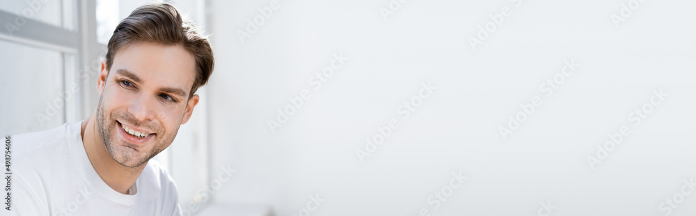 Fototapeta premium portrait of young and joyful man looking away near white wall, banner.