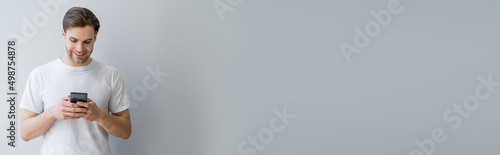 front view of happy man in white t-shirt messaging on cellphone on grey, banner. © LIGHTFIELD STUDIOS