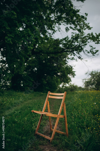 Wooden chair outdoors. Wooden folding chair for relaxation. Around the lush grass and yellow flowers.