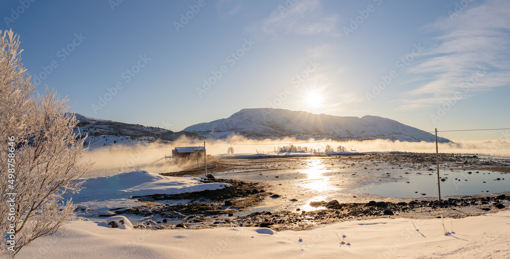 Sun rises on a frigid morning covering a house in the lake in mist
