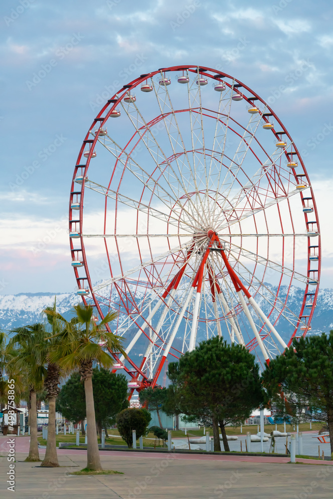 Fototapeta premium Close-up of the Ferris wheel against the background of snow-capped mountains. Beautiful city landscape, Batumi. Vertical photo