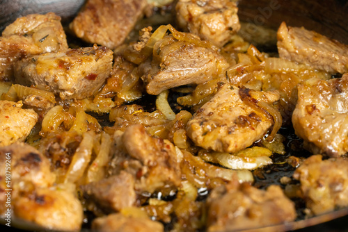 Close-up of pieces of meat with onions are fried in a frying pan.