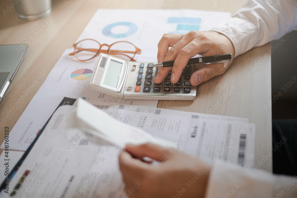 Close up hand of stress young asian businessman,male is pressing a calculator to calculate tax income and expenses, bills, credit card for payment or payday at home, office.Financial, finance concept. - obrazy, fototapety, plakaty 