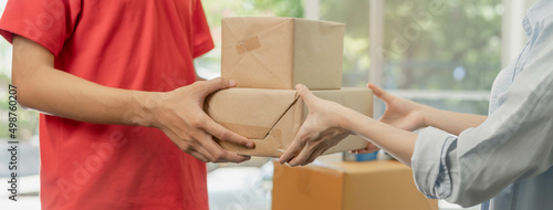 Delivery, asian young man, male postman holding cardboard box parcel, carton or mail in red uniform send to client, customer woman received from messenger, Service business, shopping online.