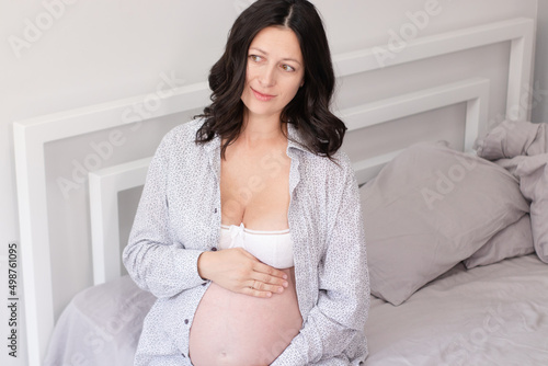 charming pregnant woman in shirt on bed. happy pregnancy