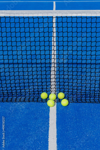 several paddle tennis balls by the net on a blue paddle tennis court © VicVaz