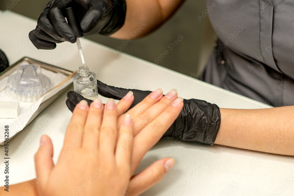 Manicure painting process. Manicure master paint the nails with transparent varnish in a nail salon, close up