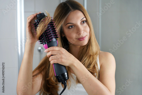 Girl using brush hair dryer to style hair at the mirror on bathroom photo