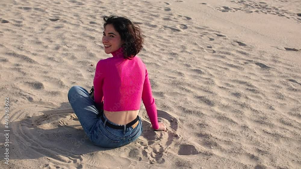 Young woman sitting on sand and laughs Young woman sitting on sand and laughs