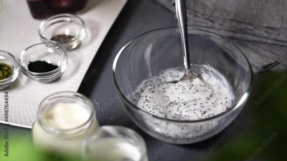 Adding maple syrup into natural yogurt with chia seeds in the glass bowl and stirring it together. Dairy product and toppings around. Making healthy breakfast Adding maple syrup into natural yogurt with chia seeds in the glass bowl and stirring it together. Dairy product and toppings around. Making healthy breakfast
