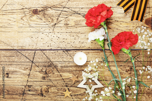 Victory Day holiday composition with bouquet of carnations, candle, stars and georgievsky ribbon on a wooden background with copy space. Anti-fascism day, Victory Day, Liberation Day photo