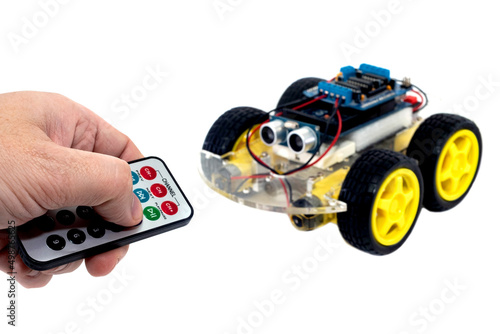 Hands using a wireless remote turn on a programmable robotic car with the ability to avoid obstacles and the ability to follow a line, isolated on a white background with clipping path. 