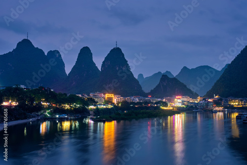 View of Yangshuo town illuminated in the evening with dramatic karst mountain landscape in background over Li river. Yangshuo, China