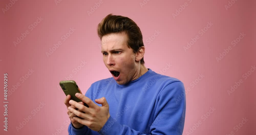 Man shocked on receiving negative news using mobile phone over pink background Man shocked on receiving negative news using mobile phone over pink background