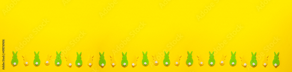 Banner of green and yellow velvet Easter bunnies on yellow background at the bottom with copy space. Flat lay top view holidays concept