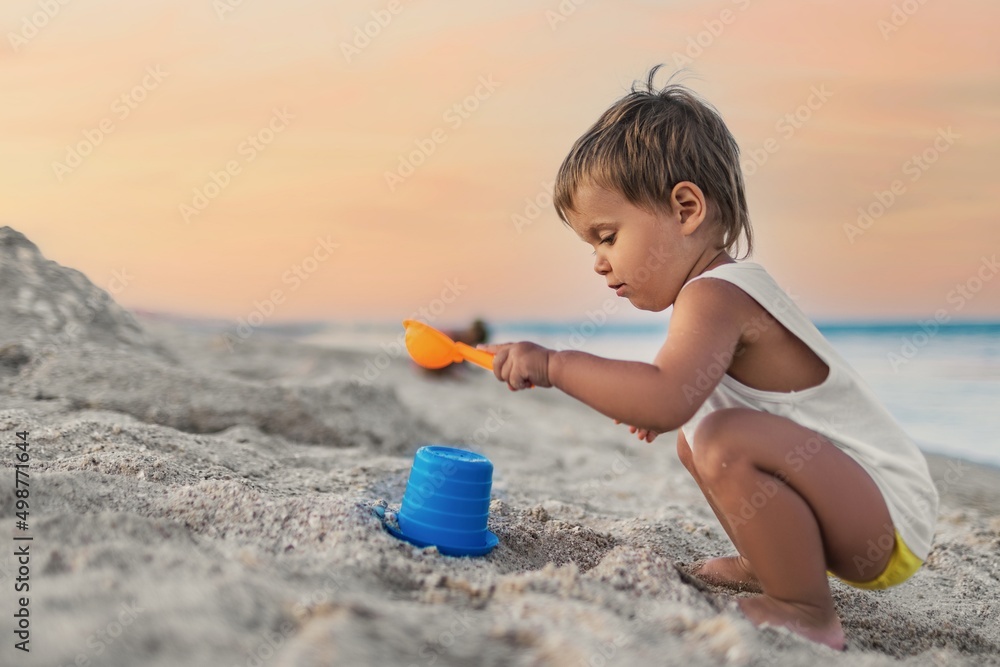 Boy playing with toys on the beach building beads and turrets smiling at someone behind the scenes on summer vacation Boy playing with toys on the beach building beads and turrets smiling at someone behind the scenes on summer vacation