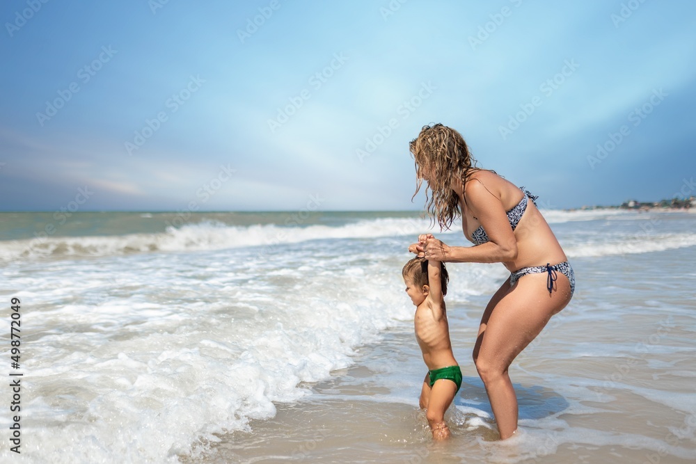 Naklejka premium Mom throws her son up over the sea on summer vacation under the warm sun