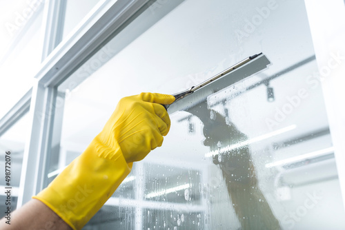 Φωτογραφία A man cleans the surface of an interior office window with a glass wiper or squeegee