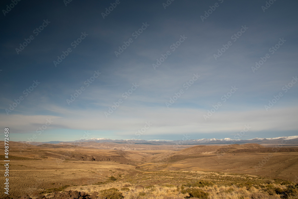 View of the golden valley and meadow under a deep blue sky. The Andes mountain range in the background.