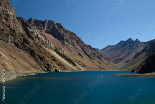 The deep blue color water lake very high in the Andes mountains. View of the Inca Lagoon in Chile, surrounded by rocky mountains and cliffs.