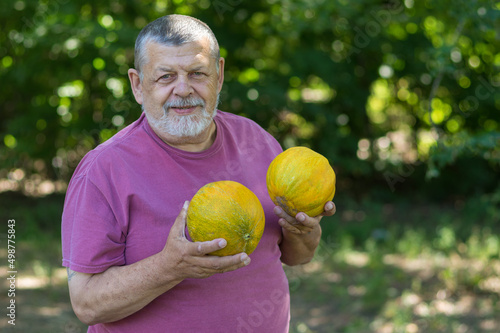 Portrait of a bearded positive Ukrainian senior farmer being happy with and holding ripe melons in hands..... © Yuri Kravchenko