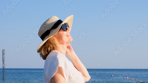 beautiful 50 year old woman in a straw hat and sunglasses on a blue sea background. Summer, vacation, vacation, active retirees