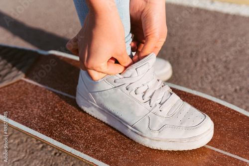 Close-up image of a woman s foot on top of a longboard tying her shoe laces. Perpendicular shot of a woman s shoe ready to go for a spin on the skate.