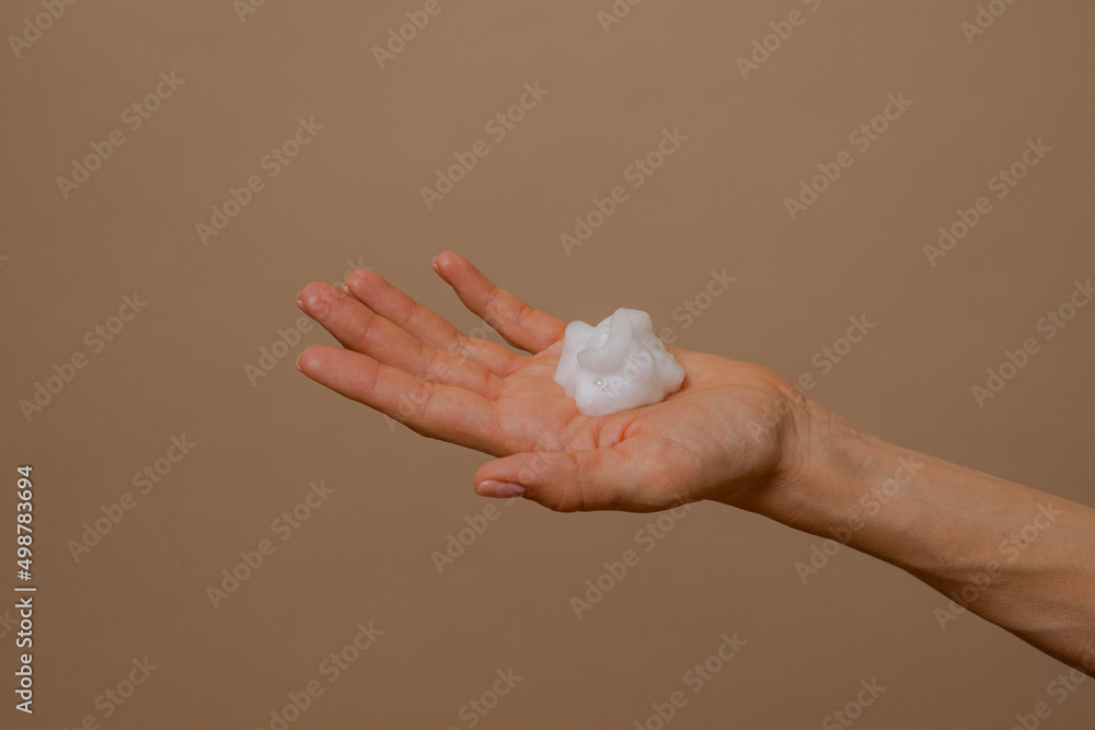 Foam for cleansing the face on a woman's palm. Facial cleansing foam. Foam in a woman's hand. White foam on a beige background. organic cosmetics Foam for cleansing the face on a woman's palm. Facial cleansing foam. Foam in a woman's hand. White foam on a beige background. organic cosmetics