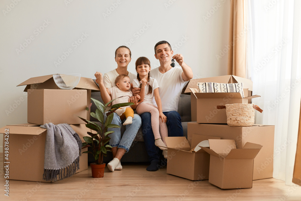 Indoor shot of happy positive family sitting on sofa with children surrounded with carton boxes, father showing to camera keys of their new apartment. Indoor shot of happy positive family sitting on sofa with children surrounded with carton boxes, father showing to camera keys of their new apartment.