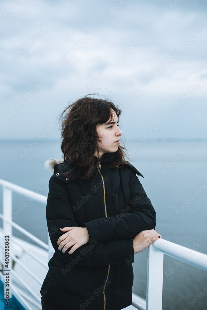 Pensive young girl looking to the sea from boat. Teenager girl at ferryboat. Cold grey sea Pensive young girl looking to the sea from boat. Teenager girl at ferryboat. Cold grey sea