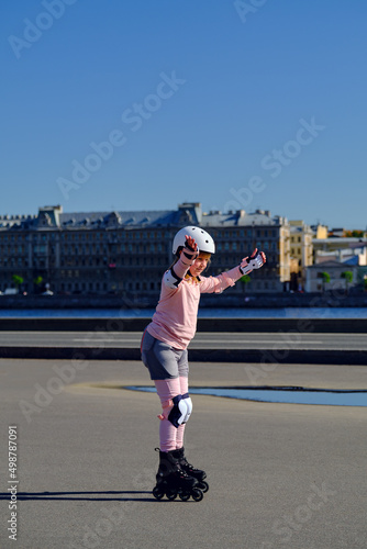 A girl in protection is rollerblading in the city. The child learns to roller skate.