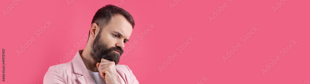Handsome man with a beard in a pink jacket is thinking over an isolated red background. Handsome man with a beard in a pink jacket is thinking over an isolated red background.