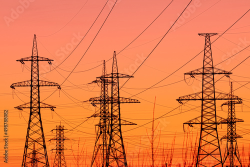 Background, view or scene of steel tower of electric main or electricity transmission line with the wires silhouette on yellow, orange and red background of sunset or sunrise sky
