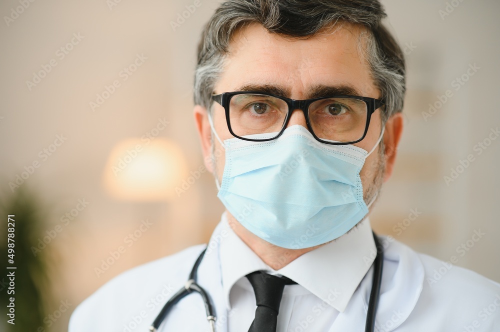 Mature old medical healthcare professional doctor wearing white coat, stethoscope, glasses and face mask. Medical staff health care protection concept. Portrait.