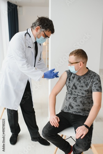 medicine  vaccination and healthcare concept - doctor wearing face protective medical mask for protection from virus disease with syringe doing injection of vaccine to male patient.