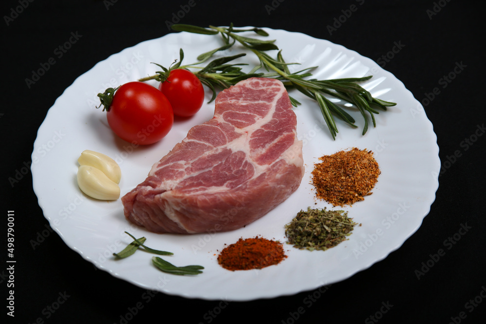 Fresh steak with spices and vegetables on a white plate and black background Fresh steak with spices and vegetables on a white plate and black background